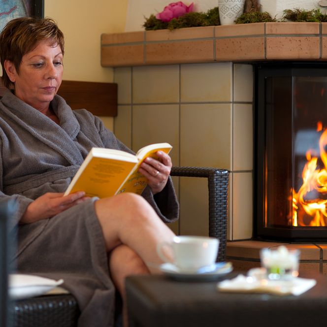Otterndorf Bistro der Saunalandschaft - Frau liest vor brennenden Kamin