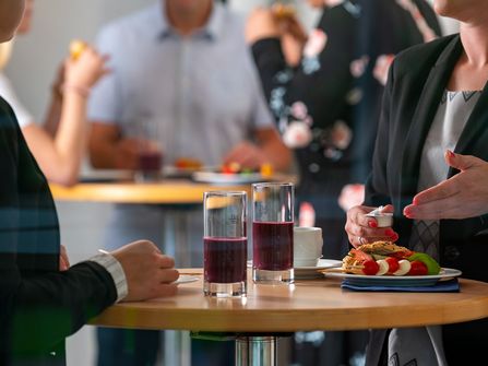 Tagungsgäste stehen an Tischen mit Essen und Getränken