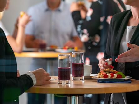 Tagungsgäste stehen an Tischen mit Essen und Getränken