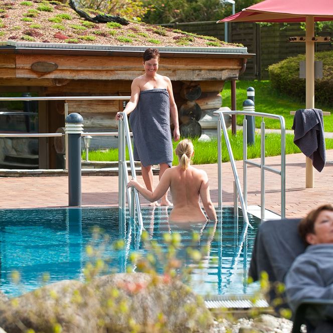 Zwei Frauen im und am Außenbecken der Saunalandschaft der Sole-Therme, eine weiter schläft im Vordergrund
