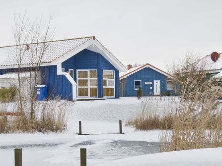 Das Bild zeigt eines der blauen Ferienhäuser im Ferienpark Südsee oder (Neu-)Seeland im Schnee.