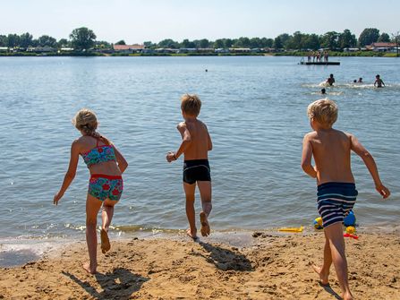 Drei Kinder rennen in den Badesee in der Freizeitanlage See Achtern Diek hinter dem Deich.