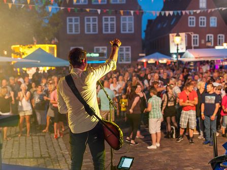 Blick von der Bühne auf den Sänger mit Gitarre und das Publikum auf dem Kirchplatz