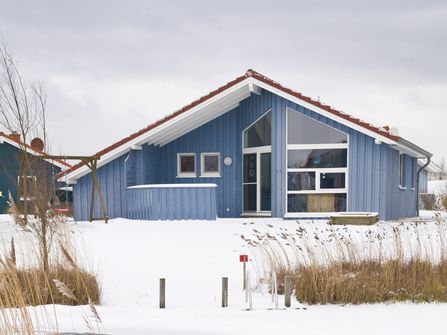 Das Bild zeigt eines der blauen Ferienhäuser im Ferienpark Südsee oder (Neu-)Seeland im Schnee.