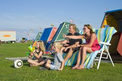 Eltern mit ihren zwei Kindern sitzen auf Klappstühlen vor einer Strandkabine