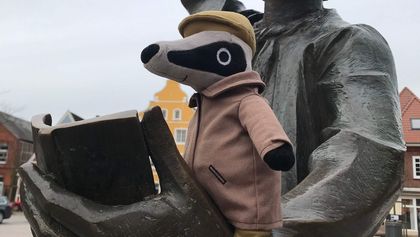 Ein Kuscheltier-Dachs sitzt auf dem Arm der Bronzestatue des Utröpers auf dem Kirchplatz in Otterndorf.